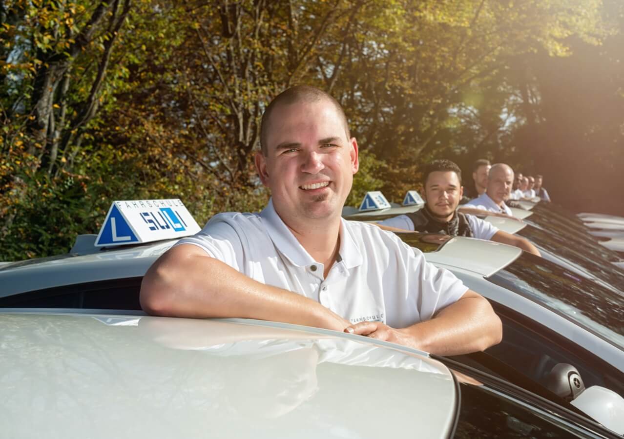 Unsere Fahrlehrer bei ihren Autos, mit Steven im Vordergrund, einem erfahrenen Mitglied des Teams.