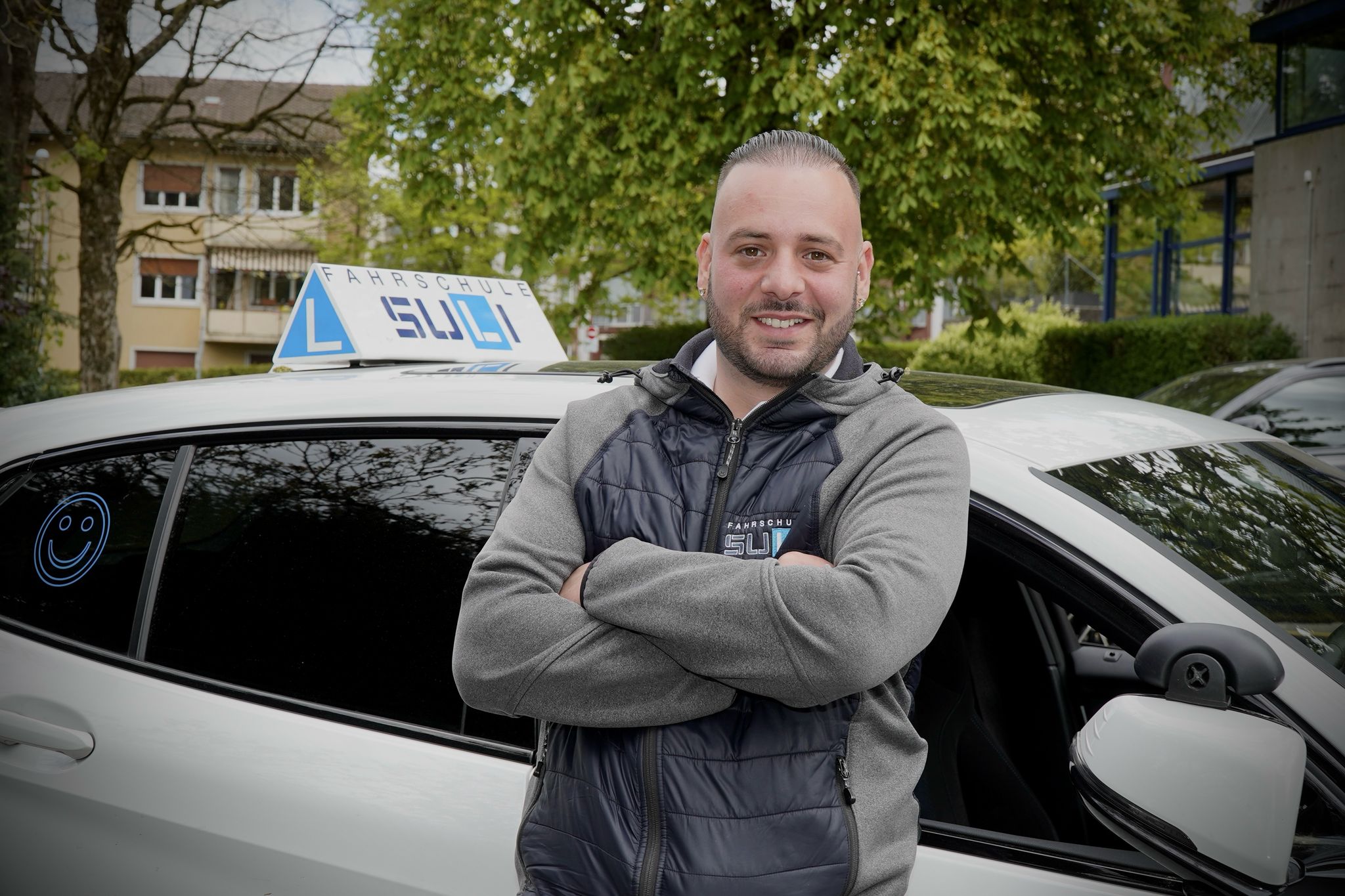 Fahrlehrer Francesco von der Fahrschule Suli lächelt in die Kamera, im Hintergrund ein Fahrschulauto.
