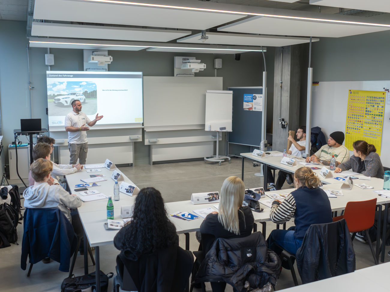 Eine Gruppe von Schülerinnen und Schülern sitzt im Klassenzimmer und hört dem Fahrlehrer während des Verkehrskundeunterrichts konzentriert zu.